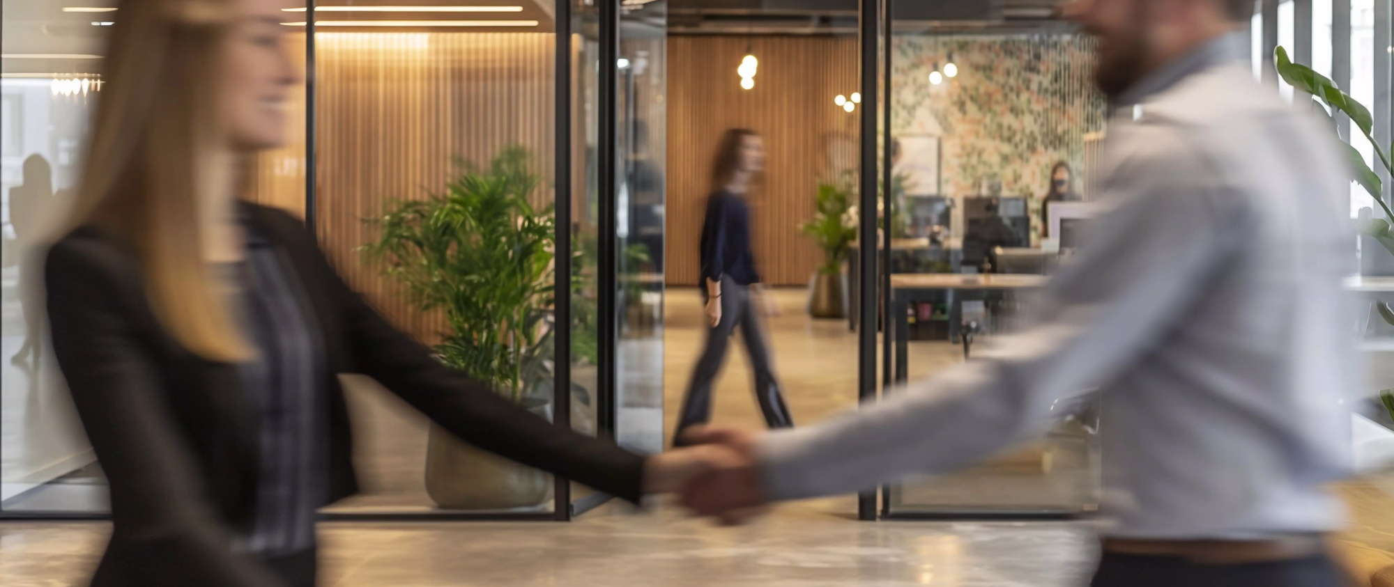 2 employés homme et femme se serrant la main avec des gens flous marchant en arrière-plan.